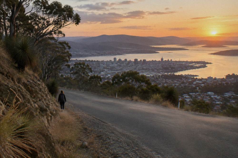 A quiet coastal road winding along the Tasmanian east coast toward orange dusk light