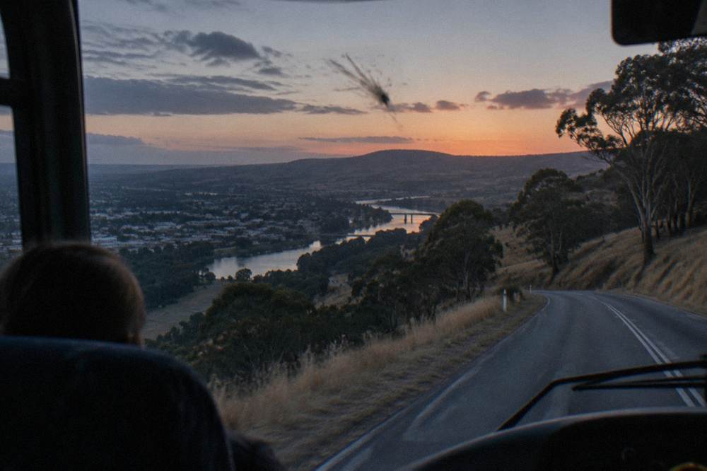 A coach parked on a quiet coastal road at dusk with headlands in the distance