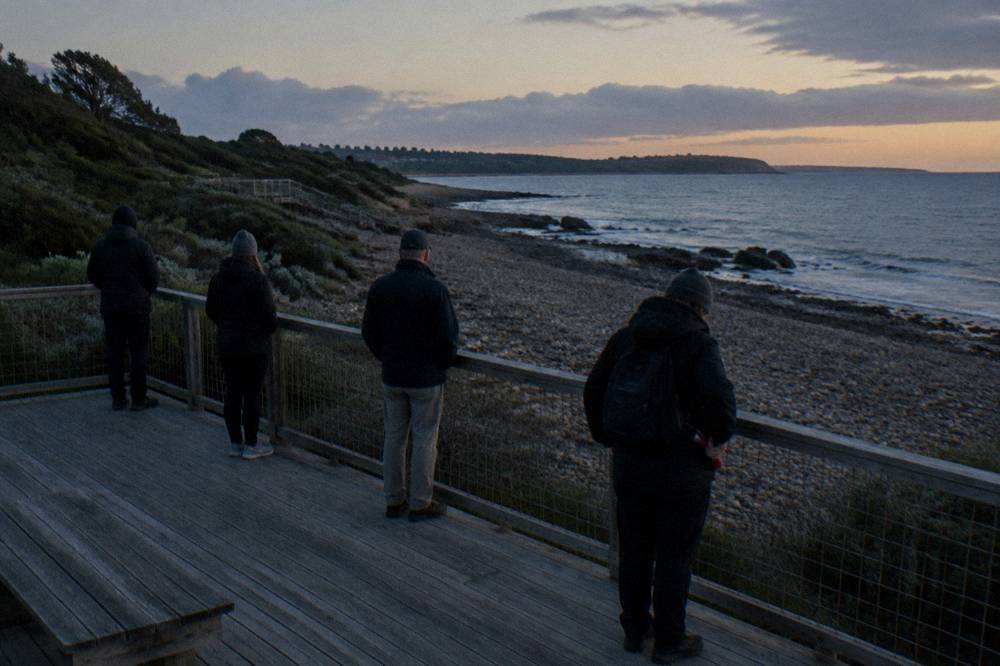 A small group of visitors standing quietly on a coastal boardwalk at dusk