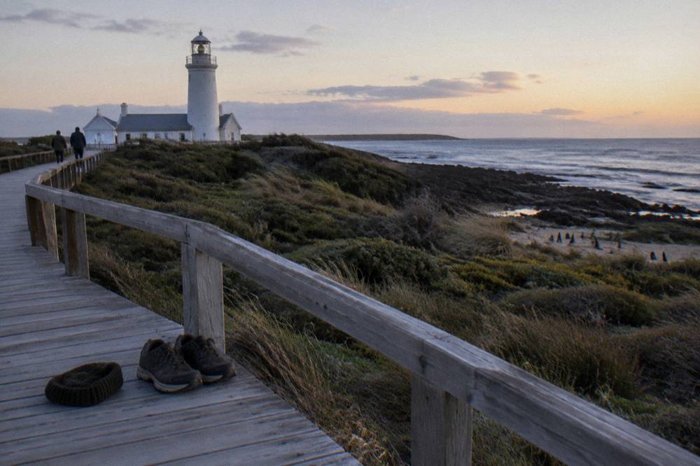 Warm jacket and enclosed walking shoes on a wooden bench near a dark beach