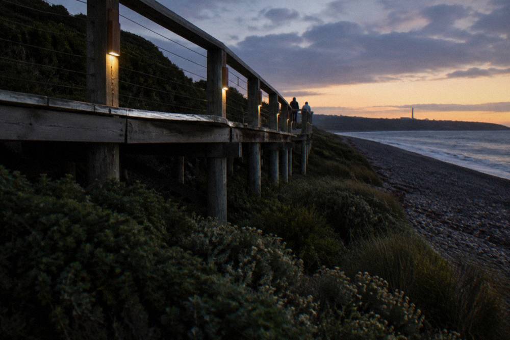A wooden viewing platform above a dark coastal reserve at twilight