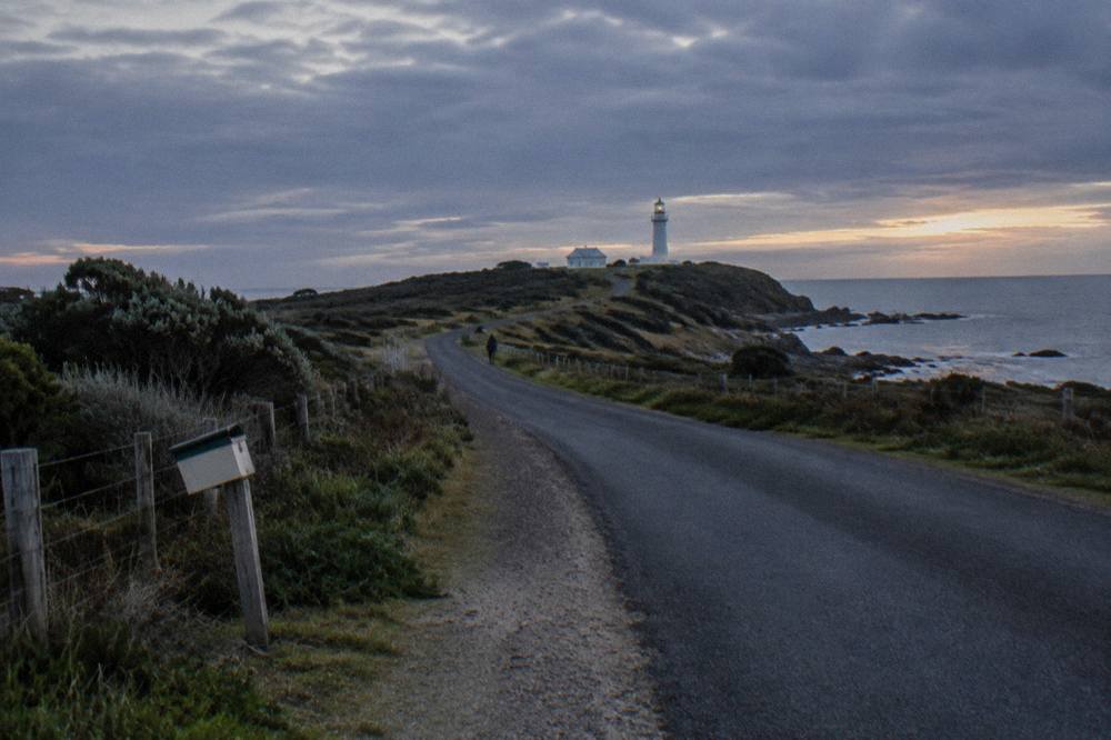 A quiet Tasmanian coastal road winding toward a dark headland in the late evening