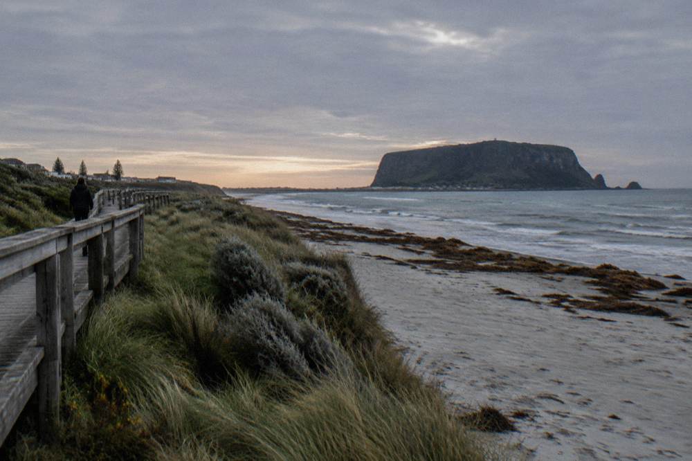 A quiet beach at last light with a raised wooden boardwalk running along the dunes behind the sand