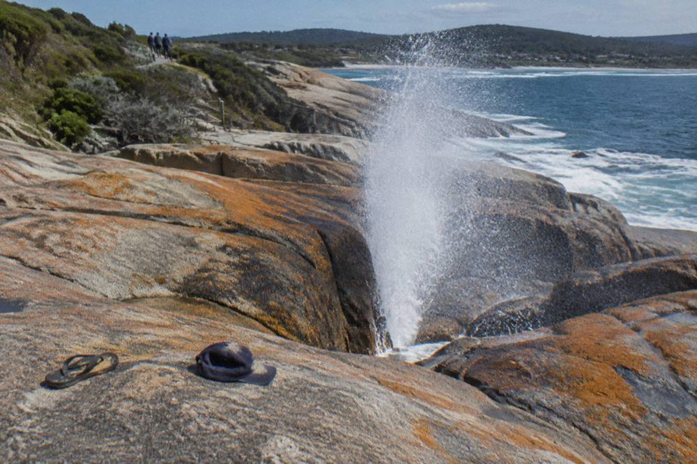 Granite rock shelf on a Tasmanian coast with white ocean spray rising from a blowhole channel