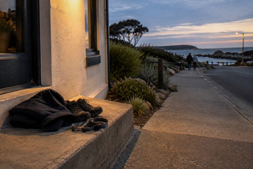 A folded jacket, scarf and sturdy walking shoes resting on a bench beside a coastal railing at dusk