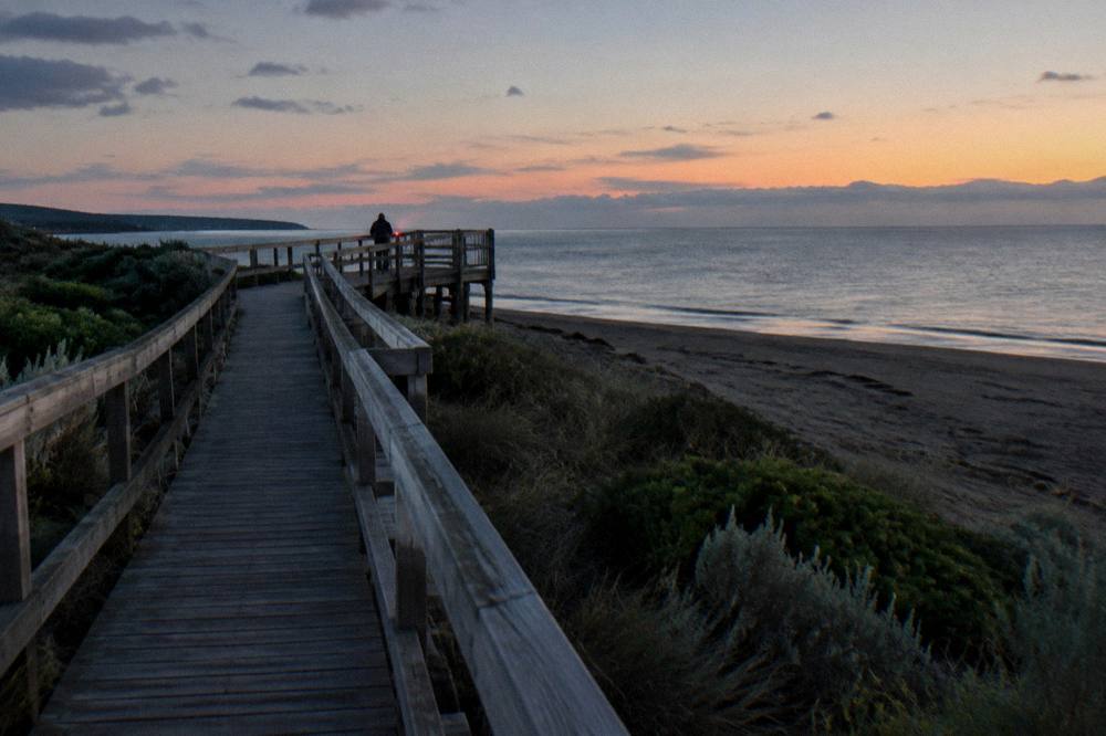 A timber boardwalk along a dark north coast beach with a small viewing platform at dusk