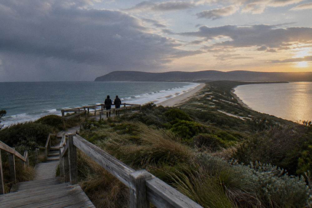 Visitors in dark jackets standing at a coastal lookout before sunset